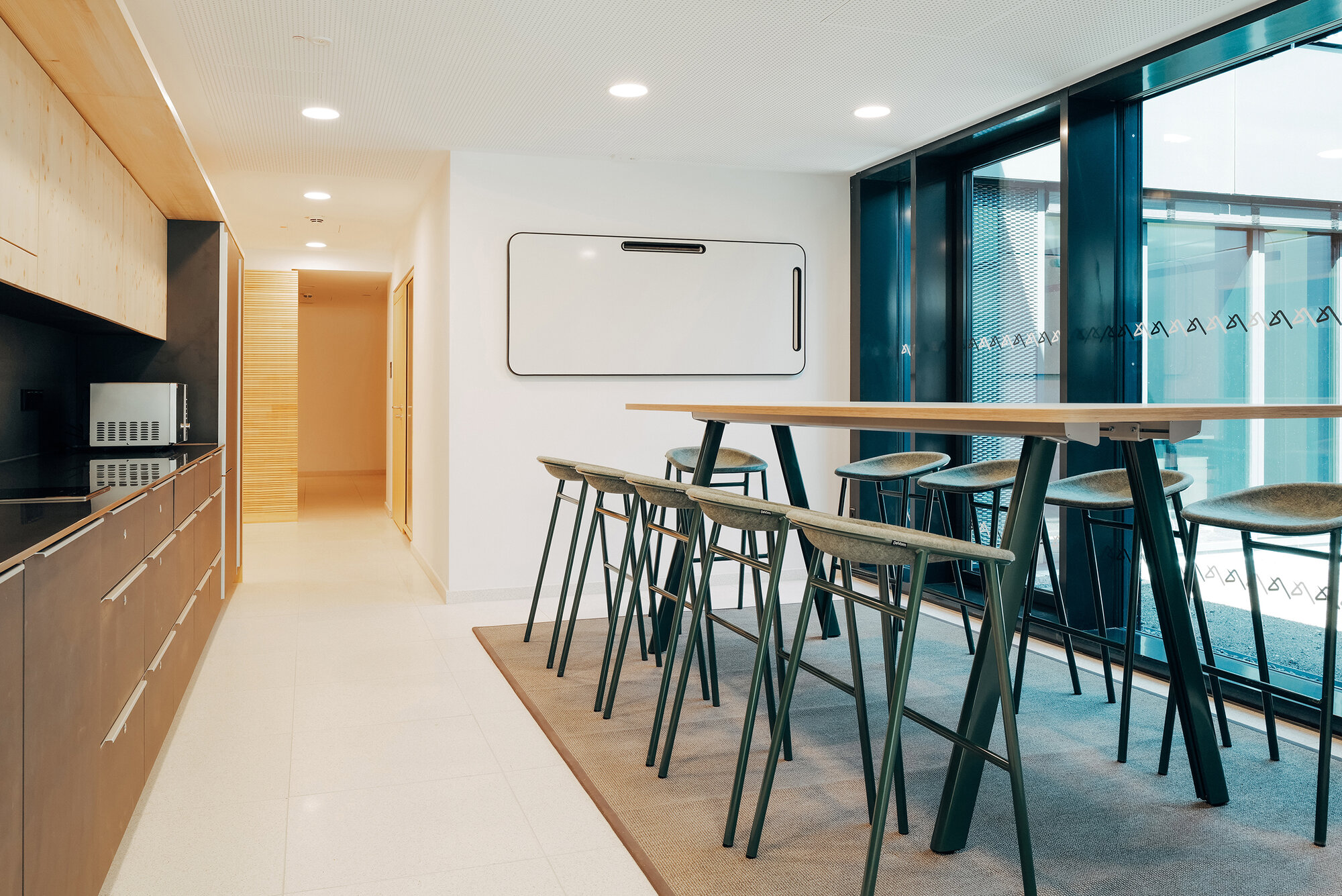 Küchenbereich im THIS mit langem Hochtisch, gepolsterten Hockern und Whiteboard